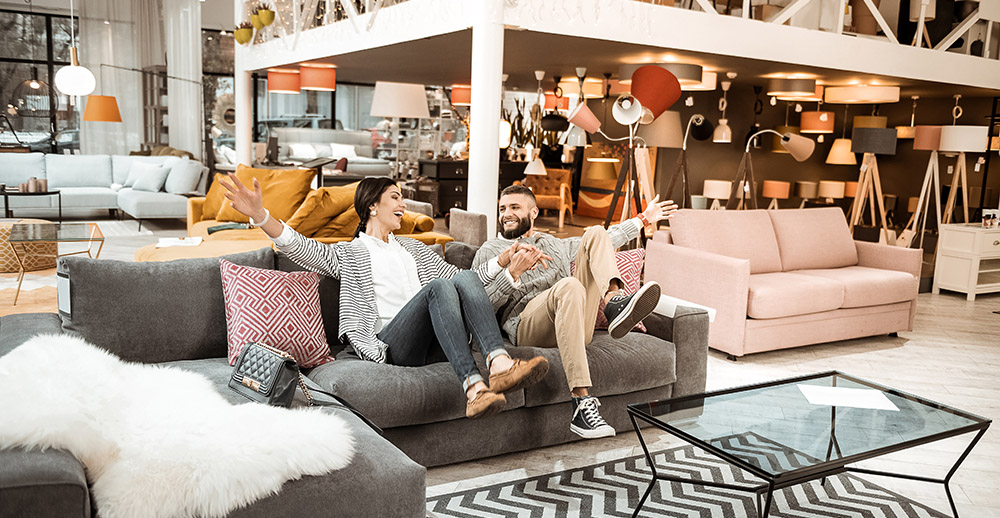 Cheerful laughing couple behaving childishly in furniture showroom making furniture shoppers happy