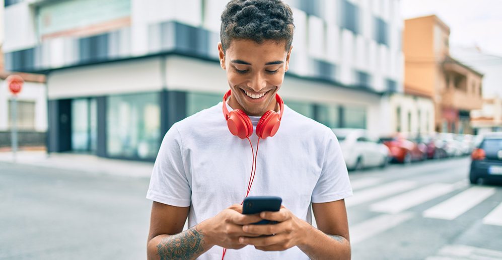 Young latin man smiling happy using smartphone and headphones at the city.