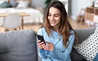 Cheerful young woman using mobile phone while sitting on a couch