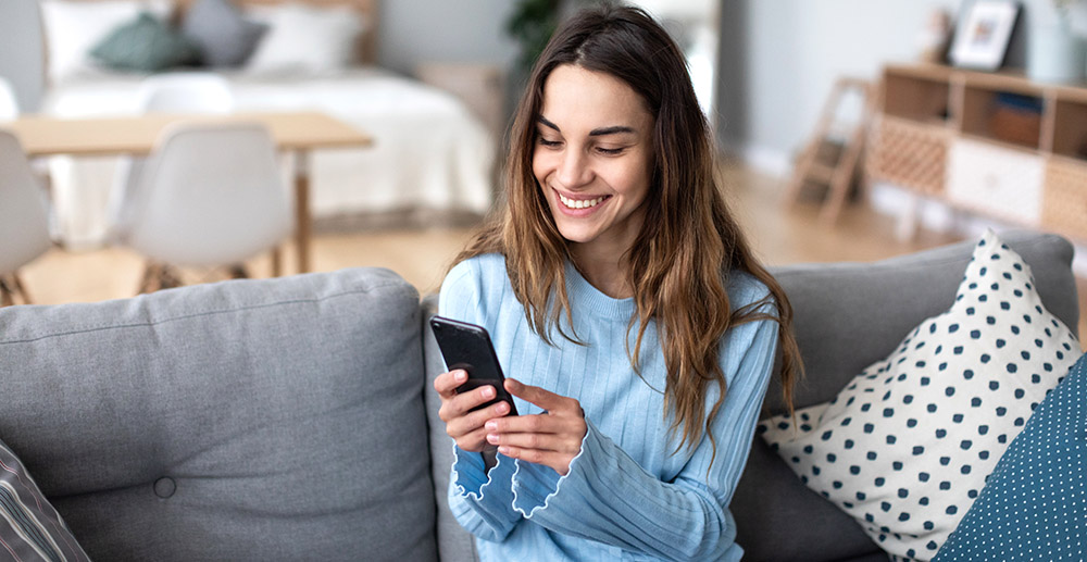 Cheerful young woman using mobile phone while sitting on a couch